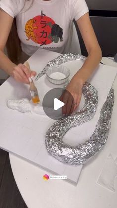 a woman sitting at a table making silver snake decorations