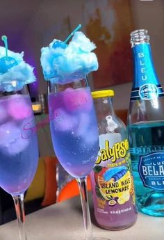 two glasses filled with blue liquid next to bottles of water and ice cream on a table