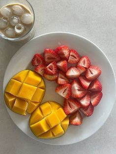 sliced strawberries and mangoes on a white plate next to a glass of milk