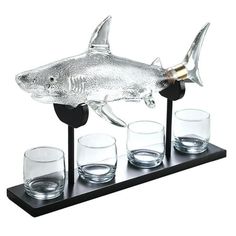 a glass shark on a black stand with four shot glasses in front of the fish