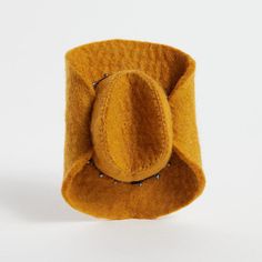 a yellow felt hat with metal studs sits on a white surface, ready to be used as a brooch