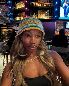 a woman wearing a knitted hat in front of a bar with neon lights on the wall