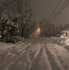 a street covered in snow at night with cars parked on the side and power lines above