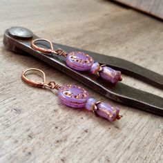 These beautiful purple earrings are sure to brighten anyone's day! These Czech glass bead compliment one another perfectly. The top bead is a 13mm purple sun wheel bead, with a bronze Picasso wash, filling in a subtle design. This is separated from the tulip bead by a 3x5 opal orange bead and a copper bead cap.The purple tulip bead has a repeat of the bronze wash on the edges of the bead, accenting the tulip shape. These earrings are also available with antique brass. Happy to put a titanium ear Vintage Purple Teardrop Earrings, Elegant Lavender Beaded Drop Earrings, Nickel-free Lavender Drop Earrings, Elegant Lavender Beaded Earrings, Purple Czech Glass Dangle Earrings, Purple Dangle Earrings With Czech Glass, Vintage Purple Drop Earrings, Bohemian Lavender Drop Earrings, Bohemian Purple Earrings Made Of Czech Glass