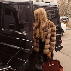 a woman in a fur coat getting out of a black suv with her handbag