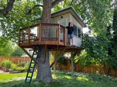 a woman standing on top of a treehouse in the middle of a green yard