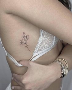 a woman's stomach with a small flower tattoo on her left side ribcage