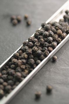 a spoon full of black pepper sitting on top of a gray table next to other spices