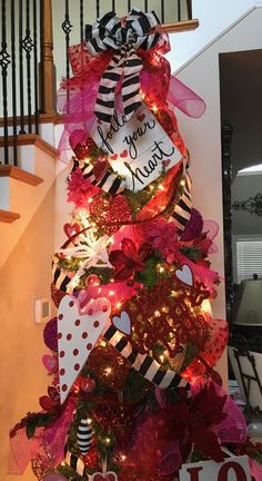 a christmas tree decorated with red, white and black ribbons is on display in front of the stairs