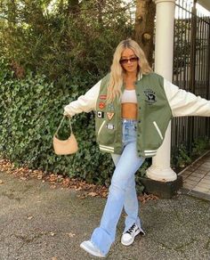 a woman standing in front of a fence with her arms spread out, wearing jeans and a jacket