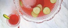 a glass bowl filled with cucumber slices next to a pitcher of watermelon juice