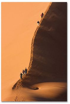 people walking up the side of a sand dune