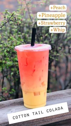 a pink and yellow drink sitting on top of a wooden table next to some trees