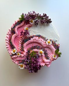 a cake with pink frosting and flowers on it sitting on a white table top