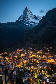 the city is lit up at night in front of a snowy mountain peak with lights on it