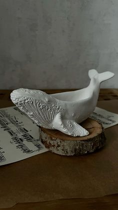 a white whale statue sitting on top of a piece of wood next to sheet music