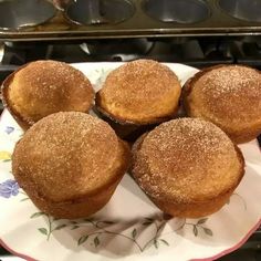 four sugary muffins on a plate in front of an oven