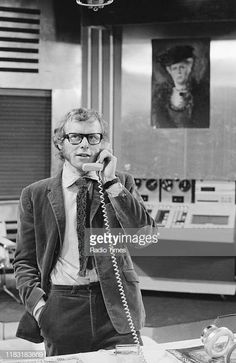 a man standing in an office talking on the phone and holding his hand up to his ear