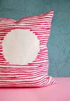 a red and white pillow sitting on top of a pink table next to a blue wall