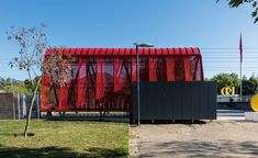 a red and black building sitting on top of a grass covered field next to a tree