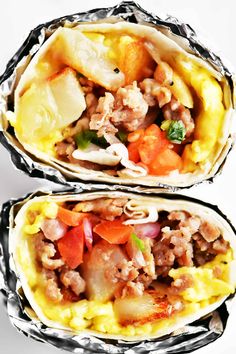 two burritos with meat and vegetables in foil wrappers on a white background