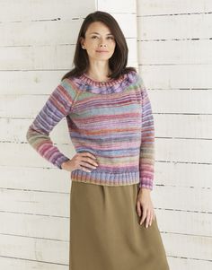 a woman standing in front of a white wall wearing a multicolored sweater and skirt