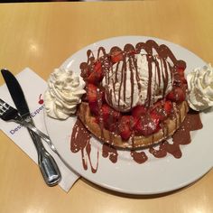 a white plate topped with waffles covered in ice cream and strawberries next to a fork