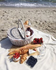 bread, berries and wine are on the beach with an ocean in the back ground