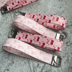 three pink and red key chains with cherries on them sitting on a gray surface