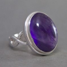 SKU: SS-036Material: 925 stamped sterling silverGemstone(s): Amethyst (N)Gemstone Dimensions: 12 X 17 X 4 mmRing Size: US 7Weight: 6.6 gramsThis remarkable Amethyst cabochon ring features a beautiful royal purple oval Amethyst in a classic bezel setting with an infinity symbol motif at the sides. This Amethyst has a depth and a glow from within that entrances the eye and lures you in. Truly a stunning stone! Spiritual Oval Amethyst Ring With Stone Setting, Oval Amethyst Gemstone With Stone Setting, Oval Sterling Silver Gemstones With Stone Setting, Oval Amethyst Ring In Silver, Oval Amethyst Ring With Sterling Silver Setting, Silver Oval Amethyst Ring, Oval Amethyst Ring With Stone Setting In Sterling Silver, Spiritual Oval Amethyst Ring For Anniversary, Oval Silver Amethyst Ring