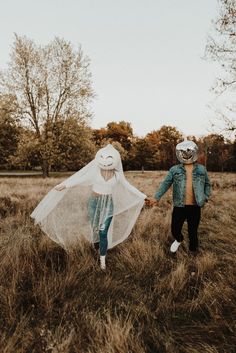 a man and woman walking through a field with a veil over their heads in front of them