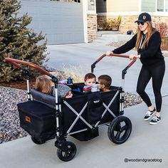 a woman pushing a stroller with two children in it and another child on the side