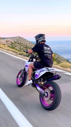 a man riding on the back of a motorcycle down a road next to the ocean