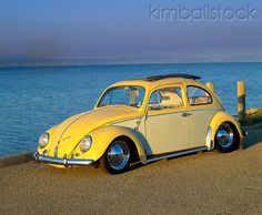 a yellow car parked on the side of a road next to the ocean with a surfboard on top