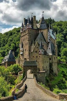 an old castle on top of a hill surrounded by trees and greenery with people walking up the walkway