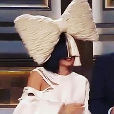 a woman wearing a white dress and big bow on her head sitting next to a man