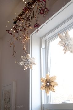 some paper stars hanging from the ceiling in front of a window with lights on them