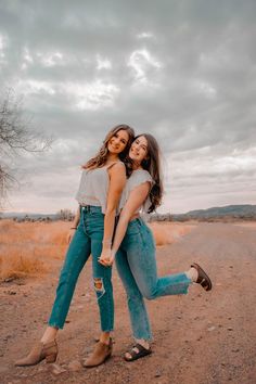 two young women are hugging in the middle of an empty dirt road, one is wearing high heeled shoes