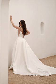 a woman in a white wedding dress leaning against a wall with her hand on her hip