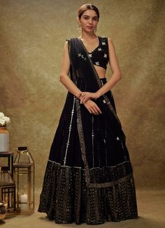 Embrace timeless elegance with the Black Mirror and Sequin Embroidered Lehenga set, a perfect blend of traditional allure and contemporary sophistication. Crafted from luxurious georgette, the flowing black lehenga is adorned with intricate gota and mirror work buttis, cascading gracefully into a striking sequin and zari embroidered border. Paired with a beautifully designed blouse, featuring mirror-embroidered buttis and accented with delicate pearl and mirror edges, this ensemble exudes opulence. The look is completed with a net dupatta, embellished with matching buttis and a coordinating border, adding an extra layer of grace. Designed for both style and convenience, this set includes a cancan for added volume and pockets for practicality, making it an ideal choice for Cocktail parties, Formal Black Pre-draped Saree With Resham Embroidery, Black Pre-draped Saree With Dupatta For Reception, Bollywood Style Georgette Lehenga For Evening, Bollywood Style Evening Lehenga In Georgette, Black Lehenga For Eid Formal Occasion, Formal Georgette Choli With Traditional Drape, Black Choli With Sheer Dupatta For Navratri, Formal Georgette Lehenga With Dupatta, Black Georgette Sharara For Festive Occasions