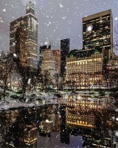 the city is lit up at night with snow falling