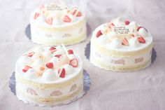 three small cakes with strawberries and cream frosting sitting on top of a table