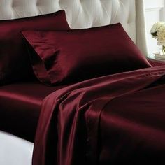 a bed covered in maroon sheets and pillows