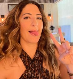 a woman making the peace sign with her fingers and wearing a leopard print top in a living room