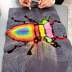 a child is drawing with colored pencils on a piece of paper that looks like a bug