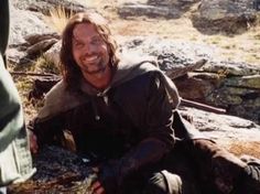 a man with long hair sitting on the ground next to a person holding something in his hand