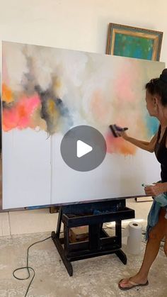 a woman is painting on an easel in front of a large white board with colorful paint