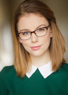 a young woman wearing glasses and a green sweater looks at the camera with an intense look on her face