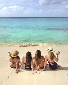 three women sitting on the beach with their backs to each other and looking out at the ocean