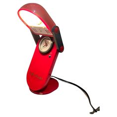 a red desk lamp with a clock on it's side and a cord attached to the base